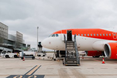 Turuncu ve beyaz uçak bulutlu bir günde bir havaalanı terminalinde yakıt dolduruluyor ve uçağa bindiriliyor.