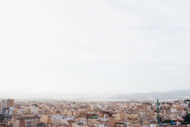 Şehir ufka doğru yayılıyor yumuşak, bulutlu bir gökyüzünün altında, uçsuz bucaksız ve puslu bir şehir yaratıyor