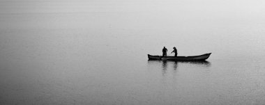 İki balıkçı, suların engin dinginliğinde yalnız bir teknede sessizce çalışır. Mannar, Sri Lanka 'da siyah ve beyaz minimalist kompozisyon. Basitlik, yalnızlık ve zamansız konsept..