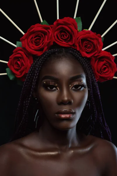 Portrait of a black woman looking at the camera, wearing red flowers on her head.Woman is looking at camera with attractive face on dark green background. Some young with flowers on her head is posing