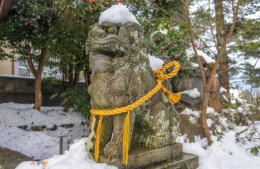 Komanu, ya da aslan-köpek, Japonya 'da Kanazawa, küçük yerel türbesindeki kutsal Shimenawa ipiyle kışın karların üzerinde heykel..