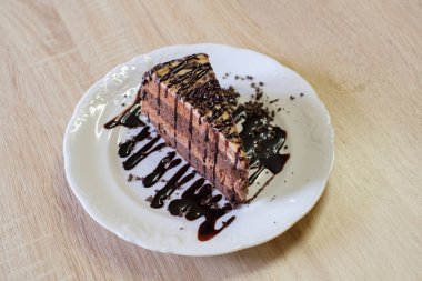 Çikolata sosu ve çikolata parçacıkları serpiştirilmiş çikolata katmanlı pasta.