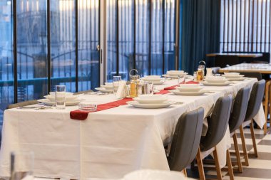 Uzun bir masa resmi bir akşam yemeği için zarif bir şekilde hazırlanır. Beyaz çarşaflar ve yer ayarları sofistike bir atmosfer yaratır.