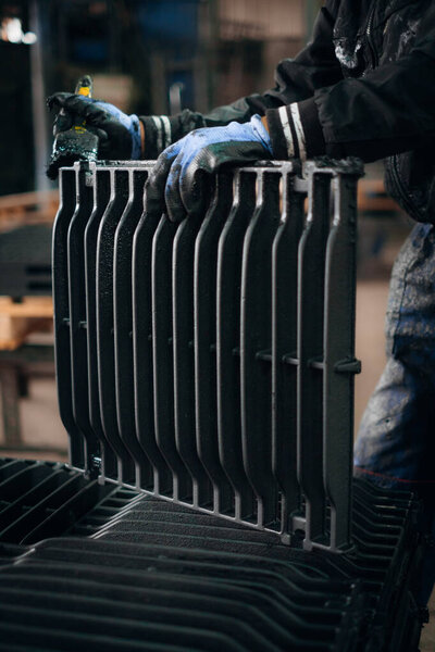 Worker applying a protective coating to a metal grate in a factory setting
