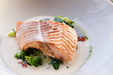 Tavada kurutulmuş somon filetosu üzerine kremalı sos, brokoli ve ıspanakla servis edilir.