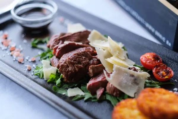 Tıraşlı parmesanlı roka ve kızarmış domatesli kurutulmuş et dilimleri.