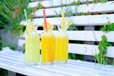 Turunçgil dilimleriyle süslenmiş beyaz bir bankta ferahlatıcı yaz içkileri.