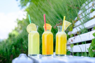 Meyve dilimleriyle süslenmiş cam şişelerdeki meyve sularını tazeliyorum.