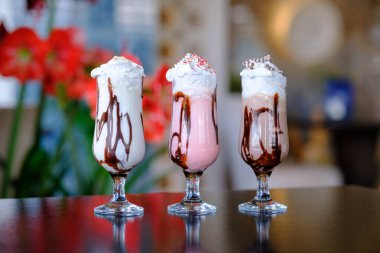 Çırpılmış krema ve çikolata sosuyla kaplı üç tane dejenere olmuş milkshake.
