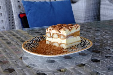 Nefis bir tiramisu dilimi kakao tozuyla kaplı bir tabağın üzerinde duruyor.