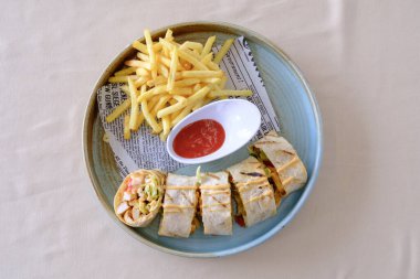 Izgara dürüm, yanında patates kızartması ve sos ile servis edilir.