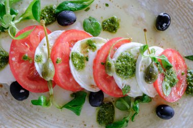 Olgun domates, kremalı mozzarella pesto ve zeytinli caprese salatası.