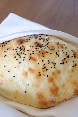 Siyah tohumlarla serpiştirilmiş sıcak, altın sarısı bir ekmek beyaz bir peçeteye nazikçe serpiştirilir.