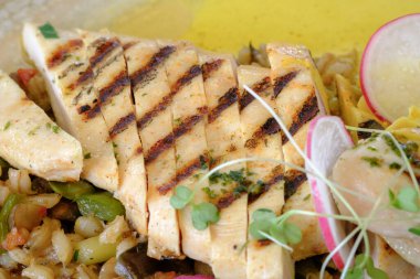 Izgara tavuk göğsü dilimlendi ve sotelenmiş sebzelerden oluşan bir yatakta servis edildi.