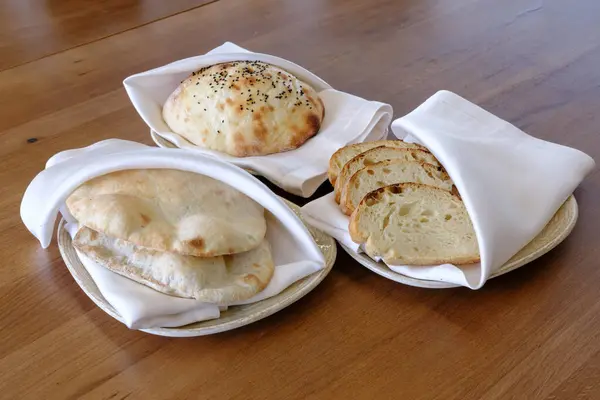 Beyaz peçetelerle servis edilen yuvarlak somunlar ve düz ekmekler de dahil olmak üzere taze ekmek çeşitleri.