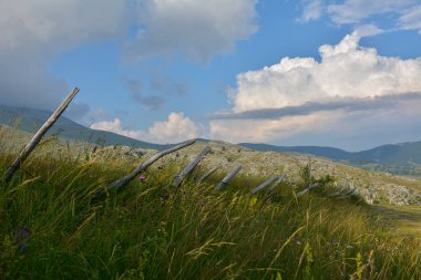 Kırsal çitler dinamik bir gökyüzünün altında dinamik bir dağ çayırında dolaşır sükuneti çağrıştırır.