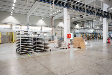 Endüstriyel ortam ve lojistik unsurları gösteren malzeme rafları ve kutuları olan geniş bir fabrika içi