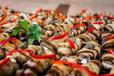 Peynirle doldurulmuş ızgara patlıcan dürümleri ve kapari ve kırmızı dolma biber parçaları.