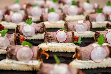 İştah açıcı et rulosu, turp ve otlarla süslenmiş karanlık bir yüzeye sanatsal bir şekilde yerleştirilmiş.
