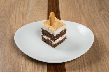 Lezzetli çok katmanlı tatlı, kremalı. Tahta tahıl masasına karşı beyaz tabakta bisküvi çubuğu dolduruyor.