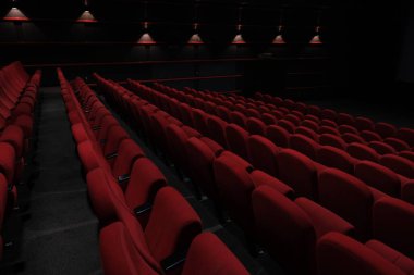 Karanlık bir tiyatroda, seyircinin gösterinin keyfini çıkarması için düzenlenmiş lüks kırmızı koltuklar.