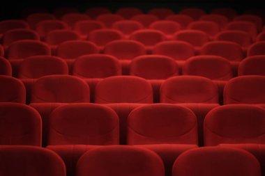 Kırmızı kadife koltuklar bir tiyatro veya oditoryum ortamında konfor ve beklenti deseni oluşturur