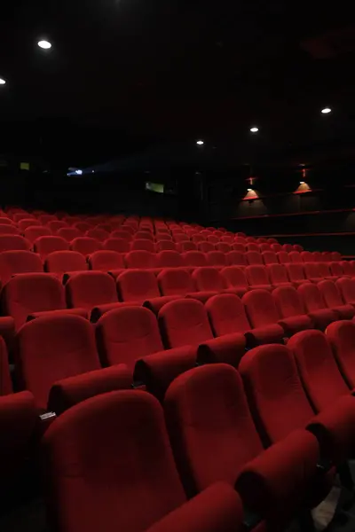 Karanlık bir salondaki kırmızı koltuklar seyirci için dramatik bir görsel model oluşturur.