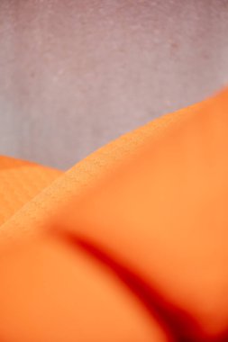 A photograph featuring the close-up texture of an orange fabric. The soft shadows and neutral-colored background provides a minimalist and artistic composition.