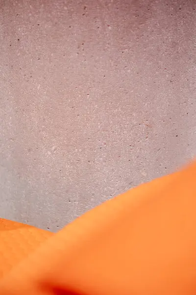 A close-up captures a textured grey surface, reminiscent of concrete, juxtaposed with a vibrant orange element, creating a visual contrast and modern aesthetic.