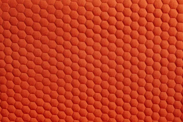A detailed close-up shot showcases an orange fabric adorned with a symmetrical honeycomb pattern. The texture and color add depth to the surface. 