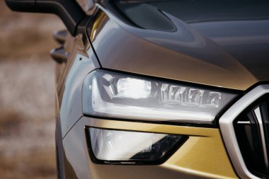 Altın bir arabanın farının detaylı görüntüsü modern tasarımı ve gelişmiş ışıklandırması dış mekândaki ışığı yansıtıyor..