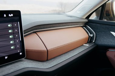Kahverengi dikişli deri süslemeli bir otomotiv panelinin yakın çekimi. Modern bir dokunmatik ekran görünür, nötr tonlu bir iç arkaplan üzerine kuruludur.