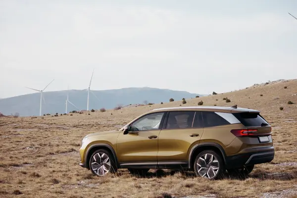 Arka planda yel değirmenleri olan bir araziye park etmiş bir SUV. Araba parlak altın renginde, dış tasarımı da şık.