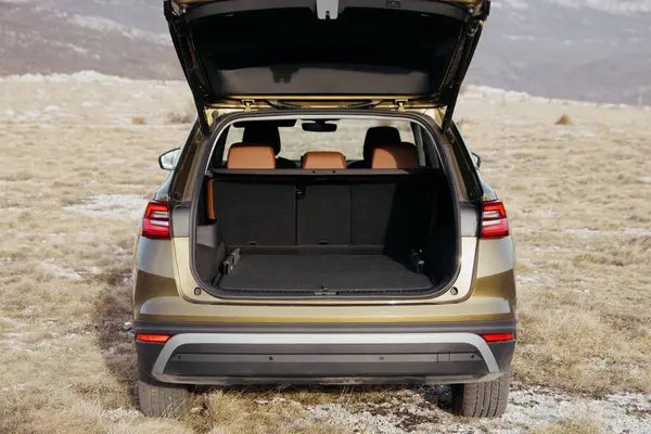 Açık bir bagaja sahip bir aracın dikiz görüntüsü, kuru çimenlerin arasına park edilmiş geniş bir kargo bölgesinin seyahat ve maceraya hazır olduğunu gösteriyor..