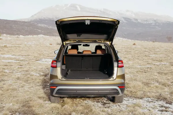 Altın rengi bir jipin arkası bagajı açık, güneşli bir günde arka planda dağlar olan çimenli bir araziye park edilmiş olarak gösterilir..