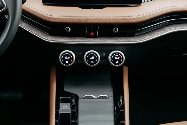 Bir arabanın merkez konsolunun yakın çekimi, klima kontrol kadranları, tehlike ışıkları, ve şık bir deri kaplama, otomatik iç mekan..