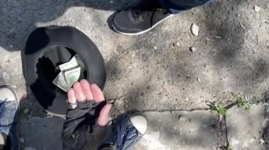 Aşağıdaki şapkalı, uzanmış elleriyle oturan evsiz adamın üst görüntüsü - para şapkasına atılır