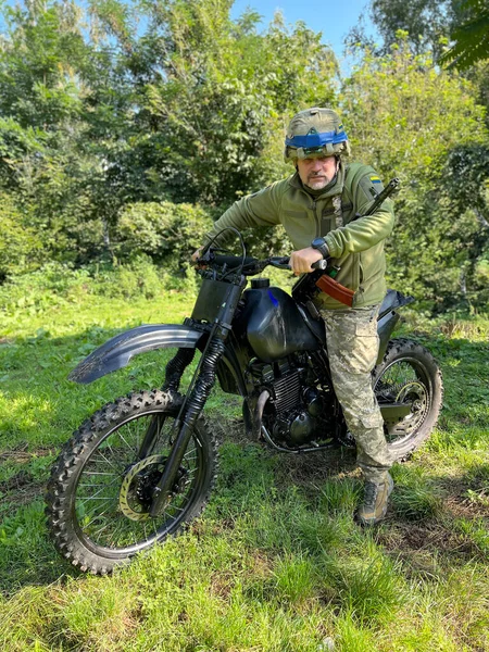 Miğferinde mavi bant, omzunda makineli tüfek, motorsiklette oturan yaşlı asker.