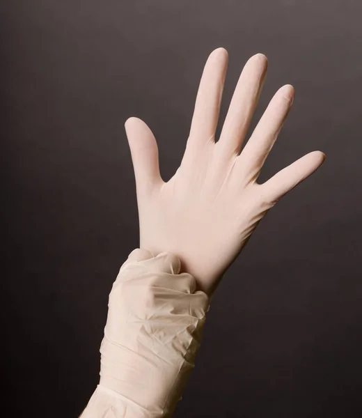 女性の手は暗い背景に白いラテックス手袋を置く — ストック写真