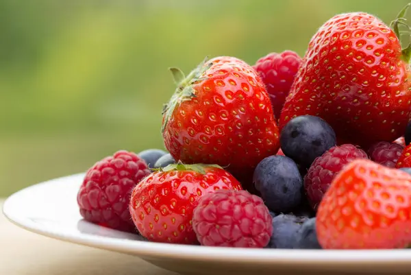 Tumpukan Stroberi Blueberry Raspberry Piring Putih Dengan Latar Belakang Hijau — Stok Foto