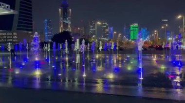 Aydınlatmalı açık havuz. Farklı renklerde su, değişen yoğunluk ve akış yönü. Arka planda bir grup insan gece su gösterisini izliyor..