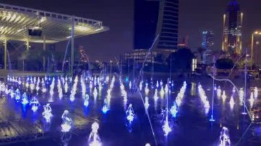 Aydınlatmalı açık havuz. Farklı renklerde su, değişen yoğunluk ve akış yönü. Arka planda bir grup insan gece su gösterisini izliyor..