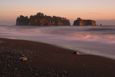 Washington Olimpiyat Ulusal Parkı 'ndaki Rialto Plajı' nda gün batımı. Arka planda deniz yığınları olan kayalık bir sahilde hareketli bulanık dalgalar.