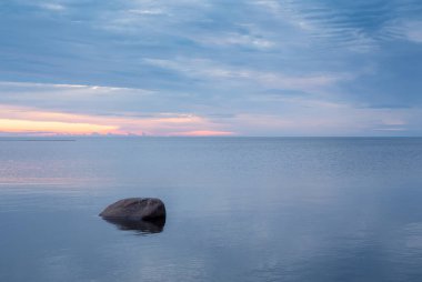 Finlandiya, Kalajoki 'de deniz suyunda duran yalnız bir kaya. Güneş arka planda güzel bir şekilde denize batar..