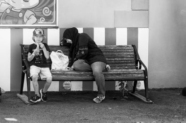 Küçük bir aile lunaparkta dinleniyor. Çocuk dondurma yiyor ve anne bugünlük yeterince eğlenmiş gibi görünüyor..
