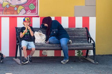 Küçük bir aile lunaparkta dinleniyor. Çocuk dondurma yiyor ve anne bugünlük yeterince eğlenmiş gibi görünüyor..