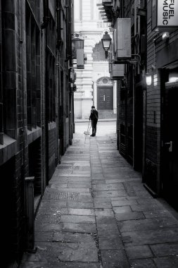 Yalnız bir temizlikçi Manchester, İngiltere 'de eski bir sokağı temizliyor. Eski fenerler duvardaki klima makinelerine zıtlık yaratıyor..