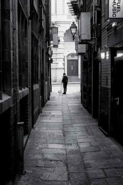 Yalnız bir temizlikçi Manchester, İngiltere 'de eski bir sokağı temizliyor. Eski fenerler duvardaki klima makinelerine zıtlık yaratıyor..