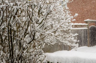 Karla kaplı ön planda kar fırtınası sırasında konut bahçesinde bir çit ve tuğla evin yanında..