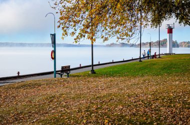 Sahil yolunda yürüyen iki kişi sabah sisinde düşen yapraklarla çevrili ve uzaktaki St. Lawrence Nehir Adaları 'nda.
